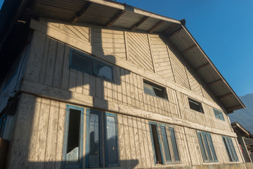 A wooden house or building early in the morning against a clear blue sky, with the sun throwing low shadows