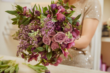 partial view of florist making bouquet of purple tulips, peonies and lilac