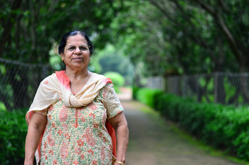 Portrait shot of a happy looking senior north Indian woman wearing traditional Indian salwar kameez in a garden against a bokeh of trees.