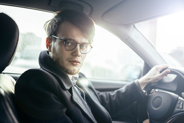 man hipster with a beard in glasses a driver of a modern car in salty weather.