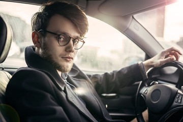 man hipster with a beard in glasses a driver of a modern car in salty weather.