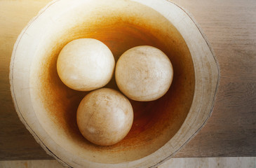 The spherical ball made of solid wood is placed in a wooden cup as well., eggs in bowl on wooden table