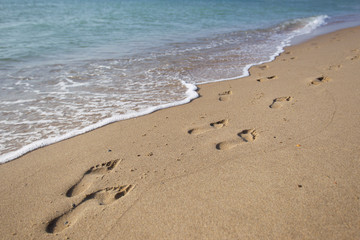 Fototapeta na wymiar Footprints in the sand against a sea wave
