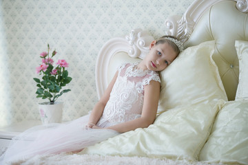 Fototapeta na wymiar Cute tender girl teenager lies on the bed. Princess in a white dress with a crown.
