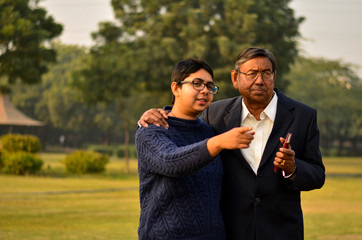 Young Indian woman with short hair with his father in an animated discussion pointing towards something in a park in Delhi, India