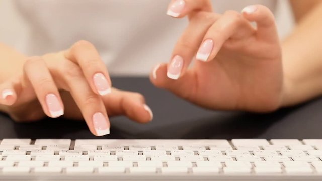 nice girl hands with light manicure enter information into computer over keyboard at black table slow motion closeup
