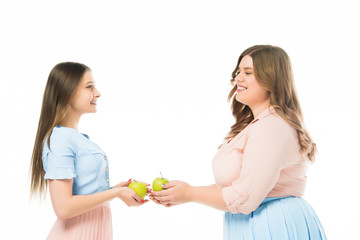 smiling elegant overweight and slim women looking at each other and holding apples isolated on white