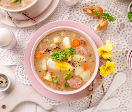 The sour soup (Żurek), polish Easter soup with the addition of sausage, hard boiled egg and vegetables in a ceramic bowl, top view. Traditional Easter dish in Poland