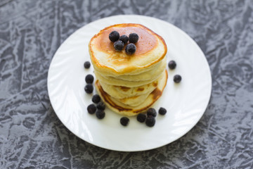 stack of pancakes with black currant berries on a gray background