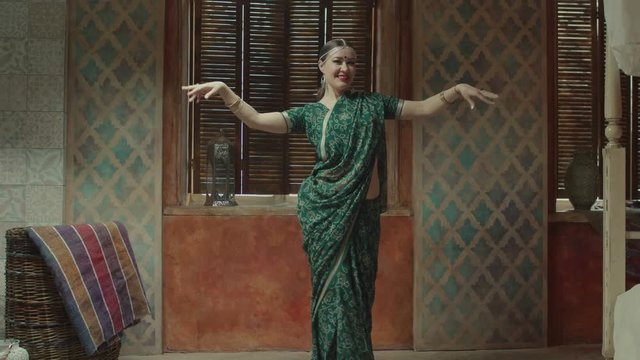 Charmingly smiling woman in ethnic indian dress saree with bindi point, bracelets and tika decoration smoothy dancing in traditional hindu manner. Female learning culture of India through dance.
