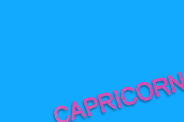 Word capricorn cut out of purple paper on blue table. Top view. Horoscope concept
