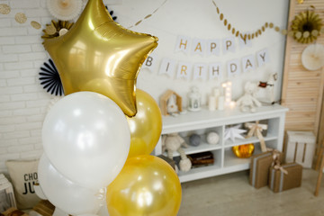 Birthday gold and silver decorations with gifts, toys, garlands and figure for little baby party on a white bricks background.