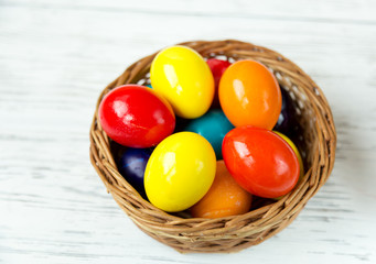 Fototapeta na wymiar Easter colored eggs in a basket on a white wooden table.