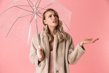 Sad confused young pretty woman posing isolated over pink wall background holding umbrella.