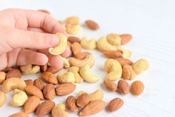 Little children fingers holding cashew nut on with selective focus and blurred heap of nuts mix on background. Roasted almond and cashew nuts for delicious protein healthy snack