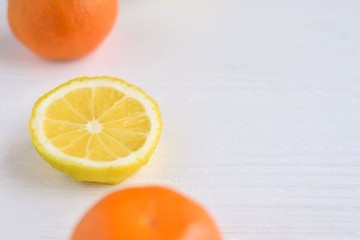 Organic orange tangerine and cut juicy yellow lemon with selective focus on white wooden table. Citrus background with empty space for text on blurred neutral backdrop. Colorful fruit flat lay 