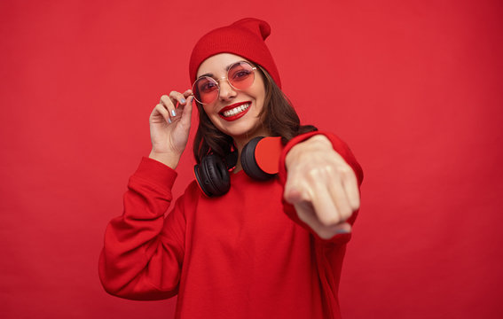 Trendy bright girl in red clothes pointing at camera 