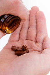 pillbottle and large brown pills in the palm of a man's hand