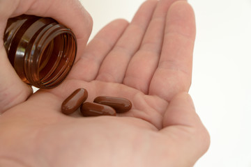 pillbottle and large brown pills in the palm of a man's hand