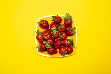 Ripe, red delicious strawberry lies in a square plate on a bright yellow background.