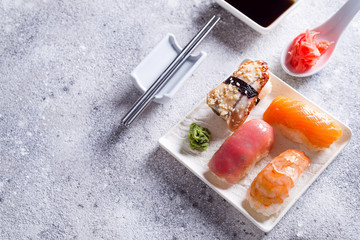 Various sushi on ceramic plate with metal Korean sticks on light stone background with green leaves, flat lay copy space