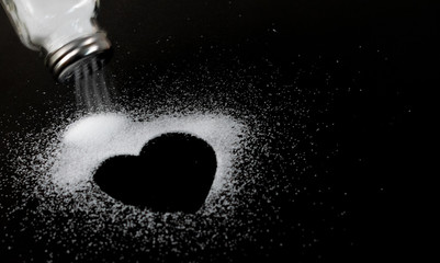 World kidney day, A white salt shaker pours out salt into the shape of heart on black paper...