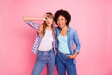 Close up photo two cheer diversity ladies different race skin tongue out mouth send kiss okay symbol fooling wear casual jeans denim checkered shirt clothes outfit isolated pink background