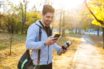 Fototapeta premium Sportsman outdoors in park listening music with earphones using mobile phone.