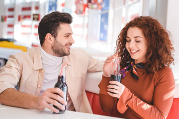  couple smiling and holding glass bottles with soda at cafe