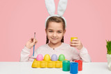 Girl in white ears coloring Easter eggs 