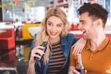 beautiful couple smiling, hugging and holding glass bottles at cafe