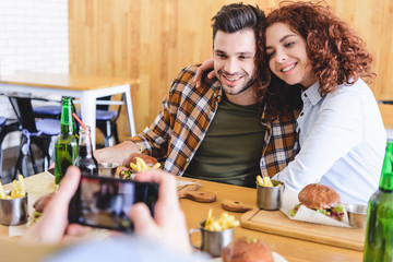 selective focus of beautiful and smiling couple posing for photo at cafe
