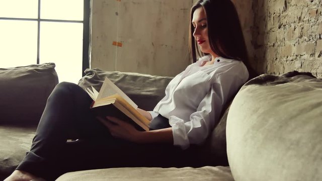 Beautiful girl sitting on the sofa. She reads a book in a cozy loft style atmosphere.