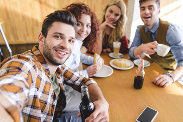 selective focus of handsome and beautiful friends smiling and looking at camera at cafe