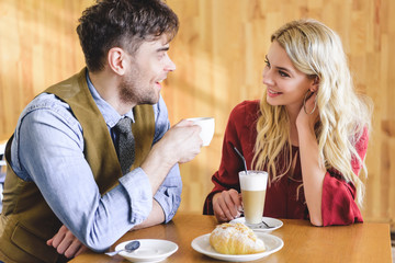 beautiful couple holding coffee cups and looking at each other