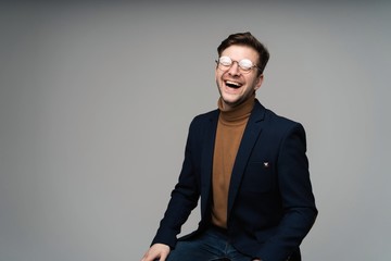 portrait of a young fashion man sitting on a chair and looking into the camera on a gray background.