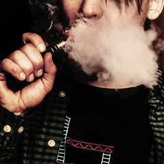 Man uses an electronic cigarette. It produces thick vapor and white smoke from the mouth.