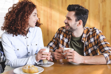 beautiful and smiling couple drinking coffee and looking at each other