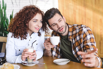 selective focus of beautiful and smiling couple drinking coffee and looking away