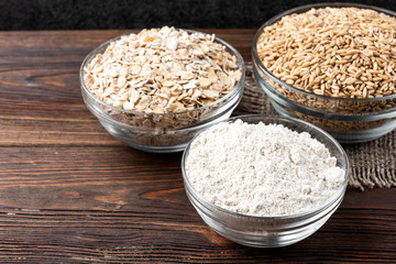 Rolled oats, oat and flour on dark wooden background.