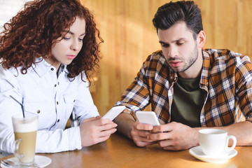 handsome man and beautiful woman using smartphone at cafe