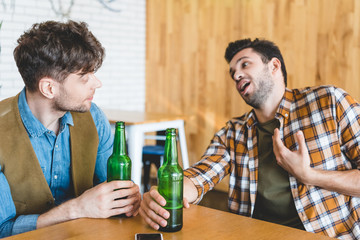 handsome men holding glass bottles of beer and talking at cafe