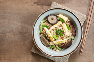 top view of stir fried instant noodle with shiitake mushroom and egg in a ceramic dish on wooden table. asian homemade style food concept.