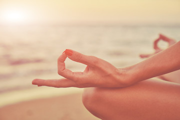 Young woman practicing yoga on the beach. Focus on hand.