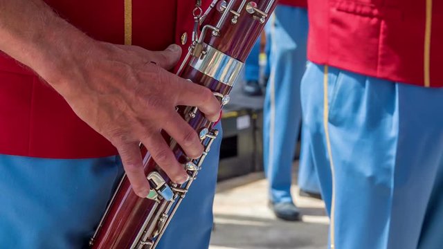 Musicians in a brass band are playin different musical instruments. They're all wearing red and blue uniforms and are entertaining the crowd.