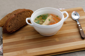 Chicken soup with green onions, and rye bread on a bamboo cutting board