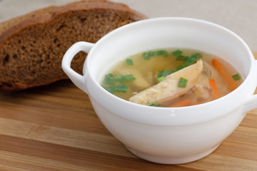Chicken soup with green onions, and rye bread on a bamboo cutting board