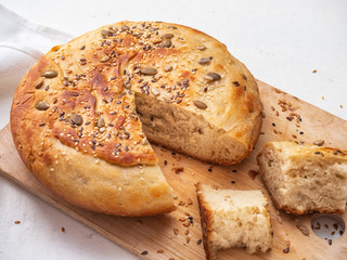 Homemade bread in cut and sliced chunks on a wooden kitchen board close-up shot, next to it is a knife with a wooden handle