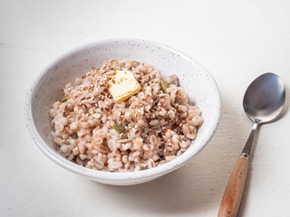 Barley porridge with a piece of butter, pumpkin and sunflower seeds, sesame seeds in a deep light ceramic plate, a teaspoon with a wooden handle on a white background is next to it, removed from close