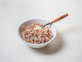 Barley porridge in a deep bowl on a white background and a teaspoon